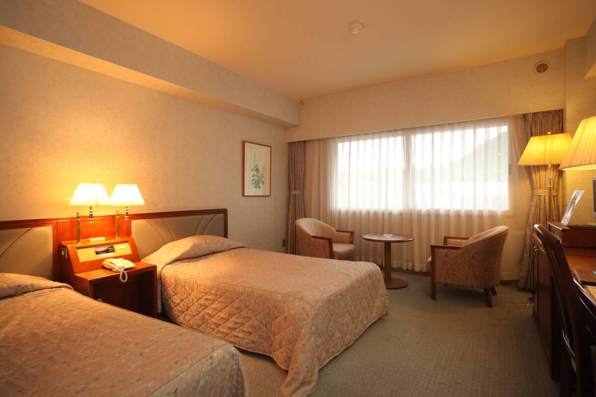 A hotel room with two beds, a desk, a chair, and a small table.