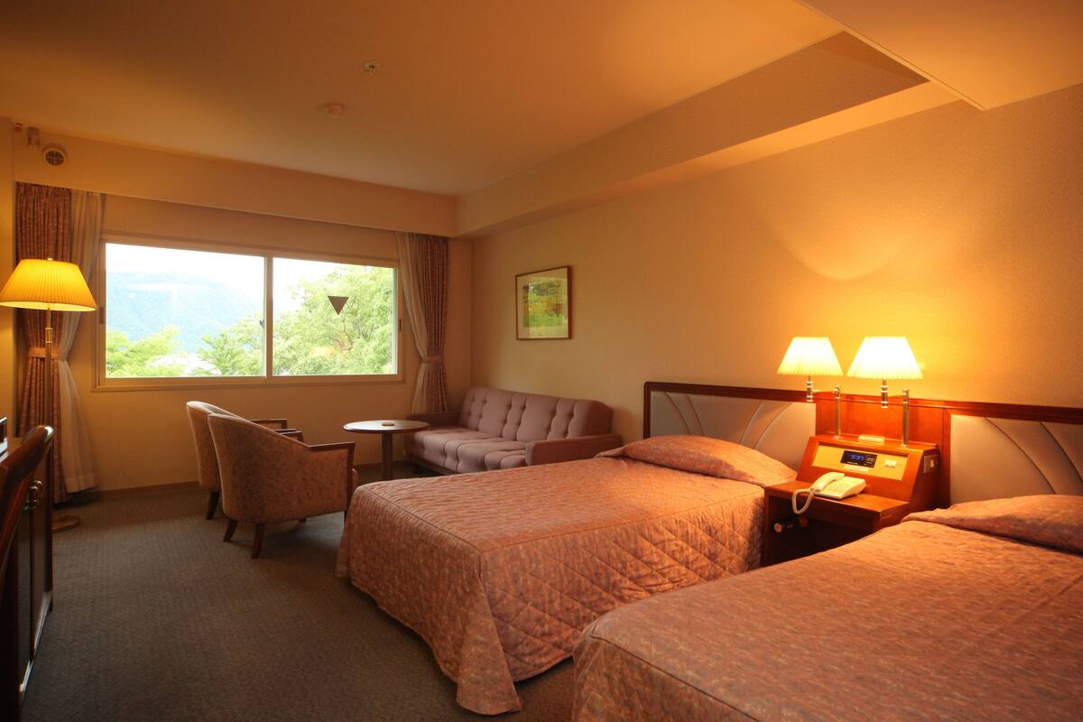 A hotel room with two beds, a sofa, a small table, and a lamp.