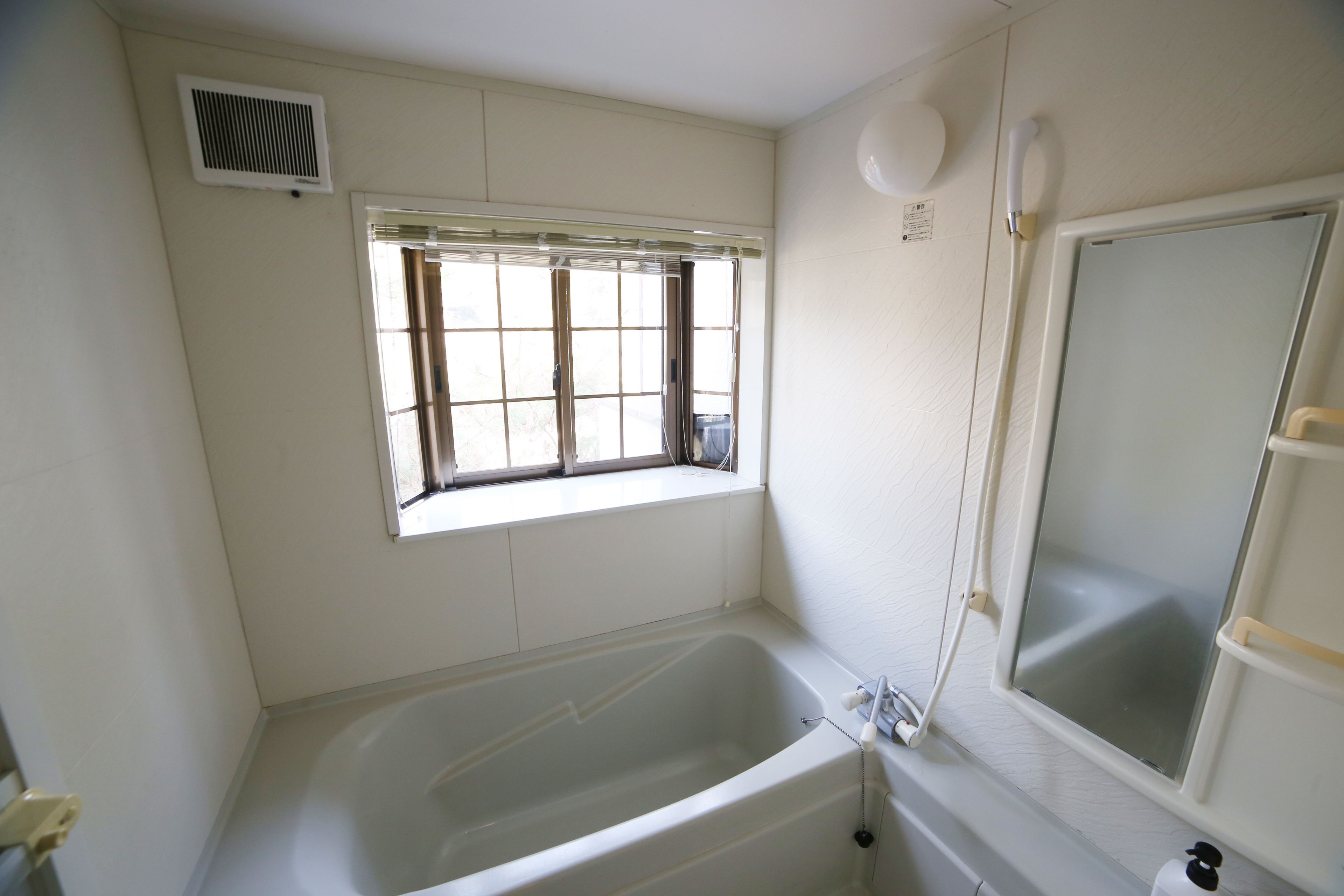 A bathroom with a bathtub, a window with blinds, a shower area, and a toilet.