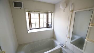 A bathroom with a bathtub, a window with blinds, a shower area, and a toilet.