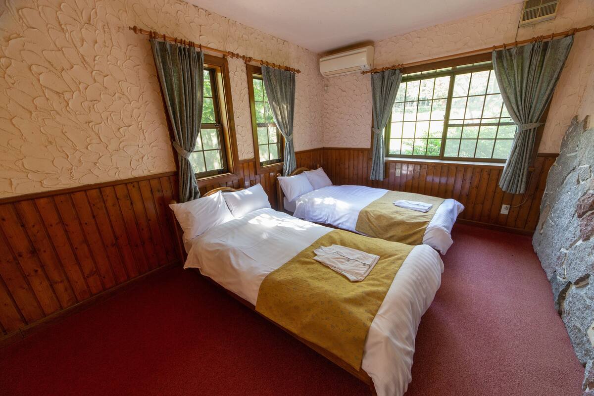 Una habitación con dos camas, paneles de madera, alfombra roja y pared de piedra.