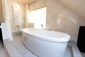 Een moderne badkamer met een vrijstaand bad, een douchecabine van glas en een groot raam voor natuurlijk lichtinval.