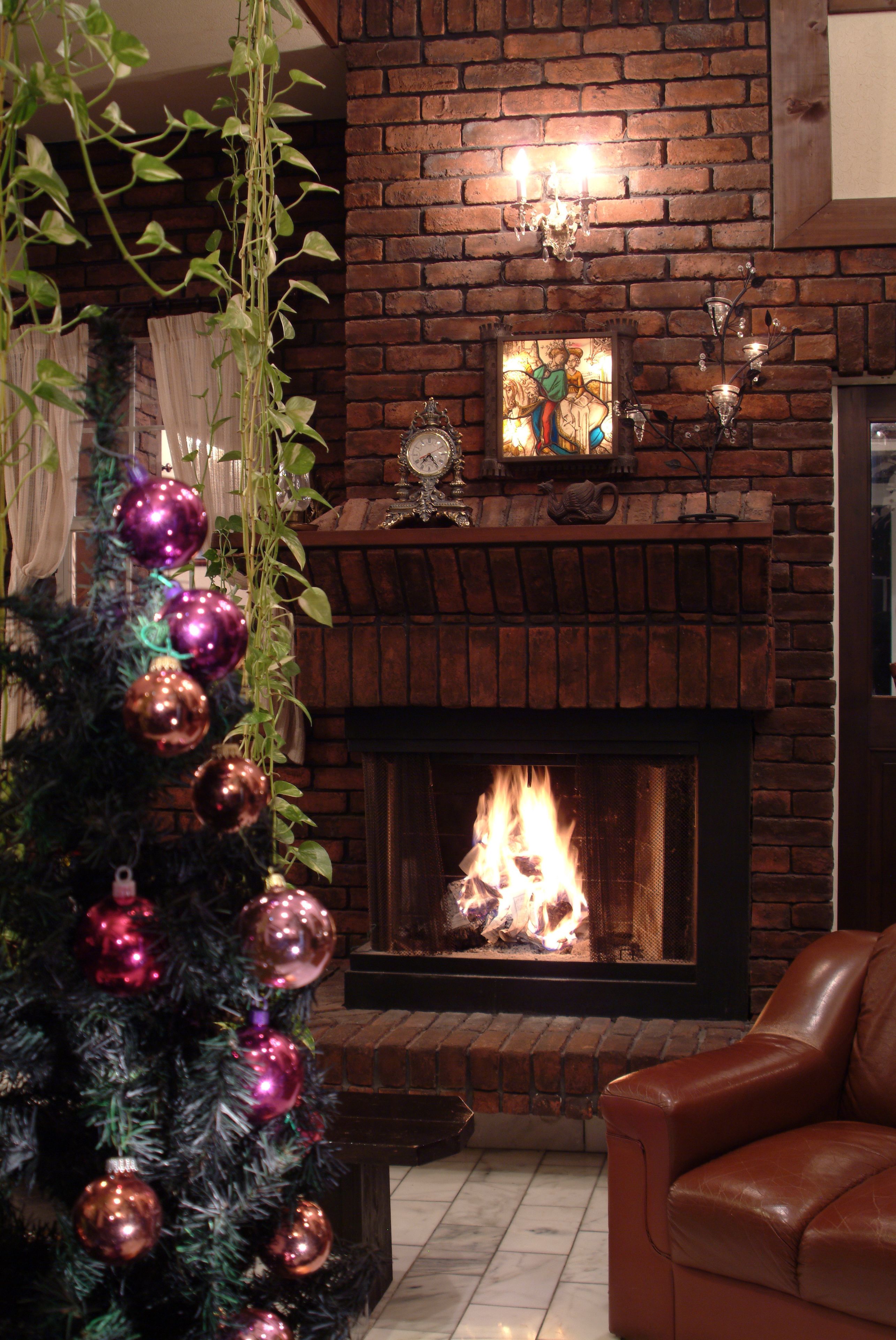 A fireplace with a brick surround, a Christmas tree with ornaments, and a leather armchair.