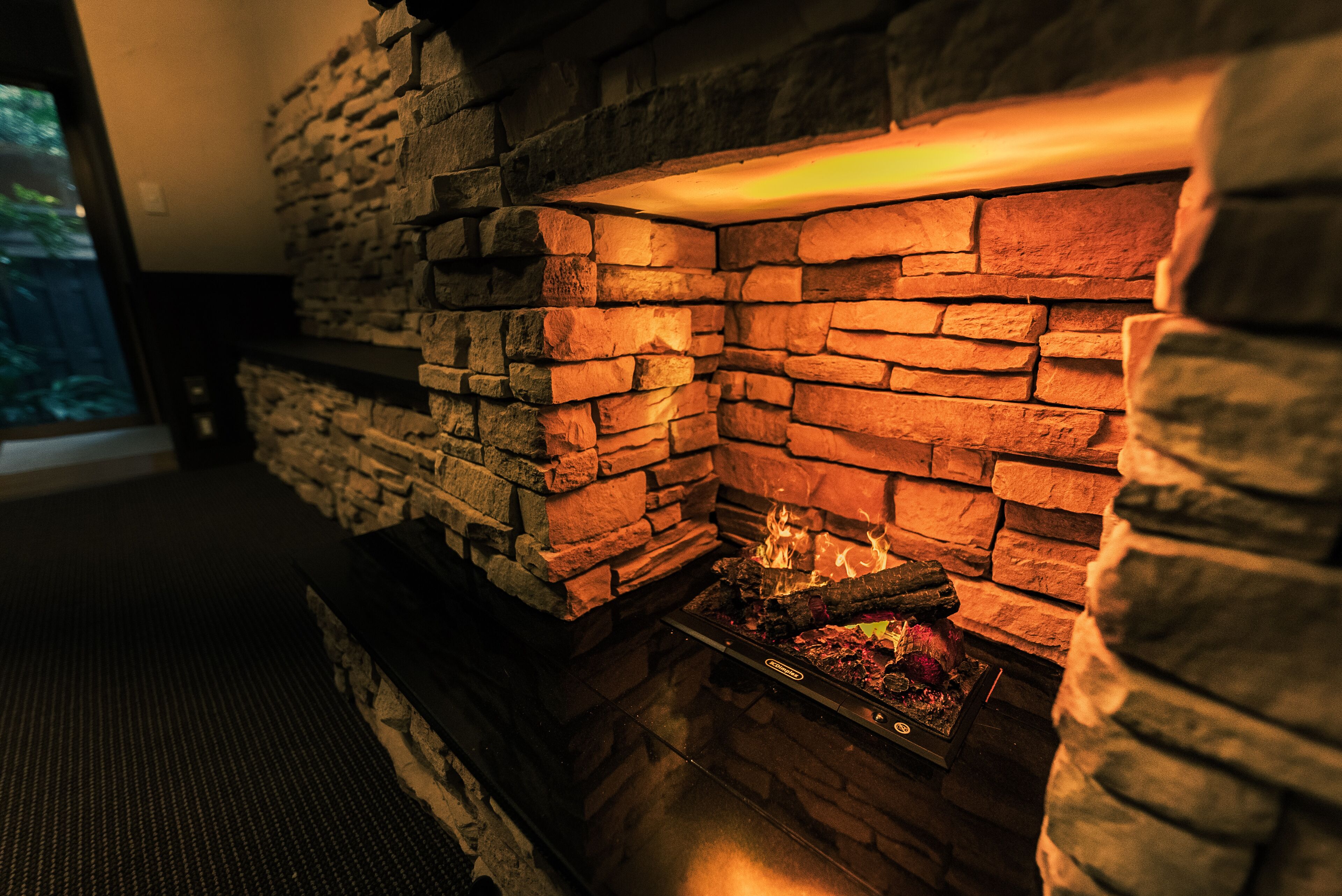 A stone fireplace with a fire burning inside, a window to the left, and a dark floor.