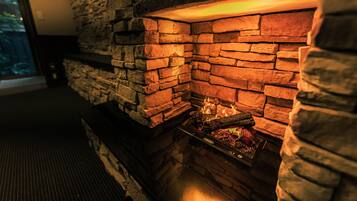 A stone fireplace with a fire burning inside, a window to the left, and a dark floor.