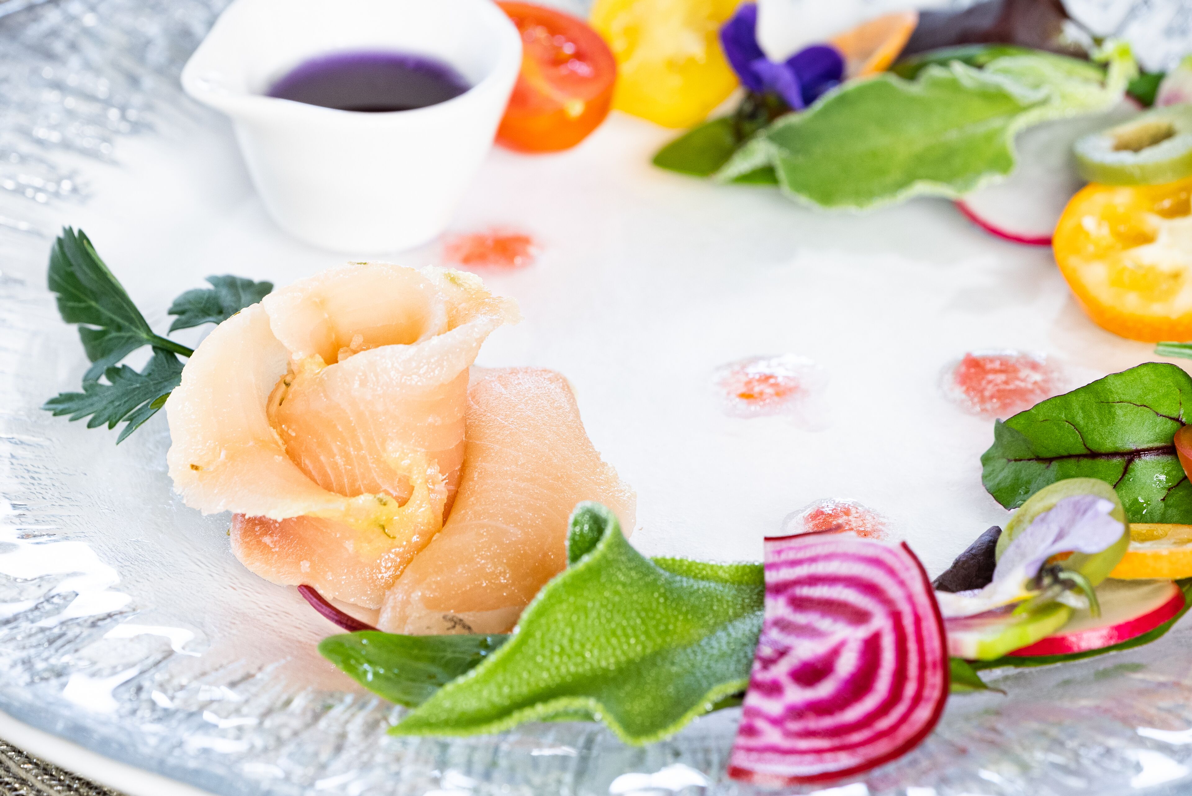 Une assiette de saumon fumé, un petit bol de sauce et un assortiment de légumes frais.