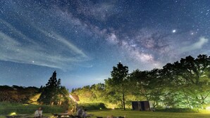 Cielo estrellado con gente recostada en sillas de jardín en un espacio abierto y cubierto de césped, bajo un cielo despejado.