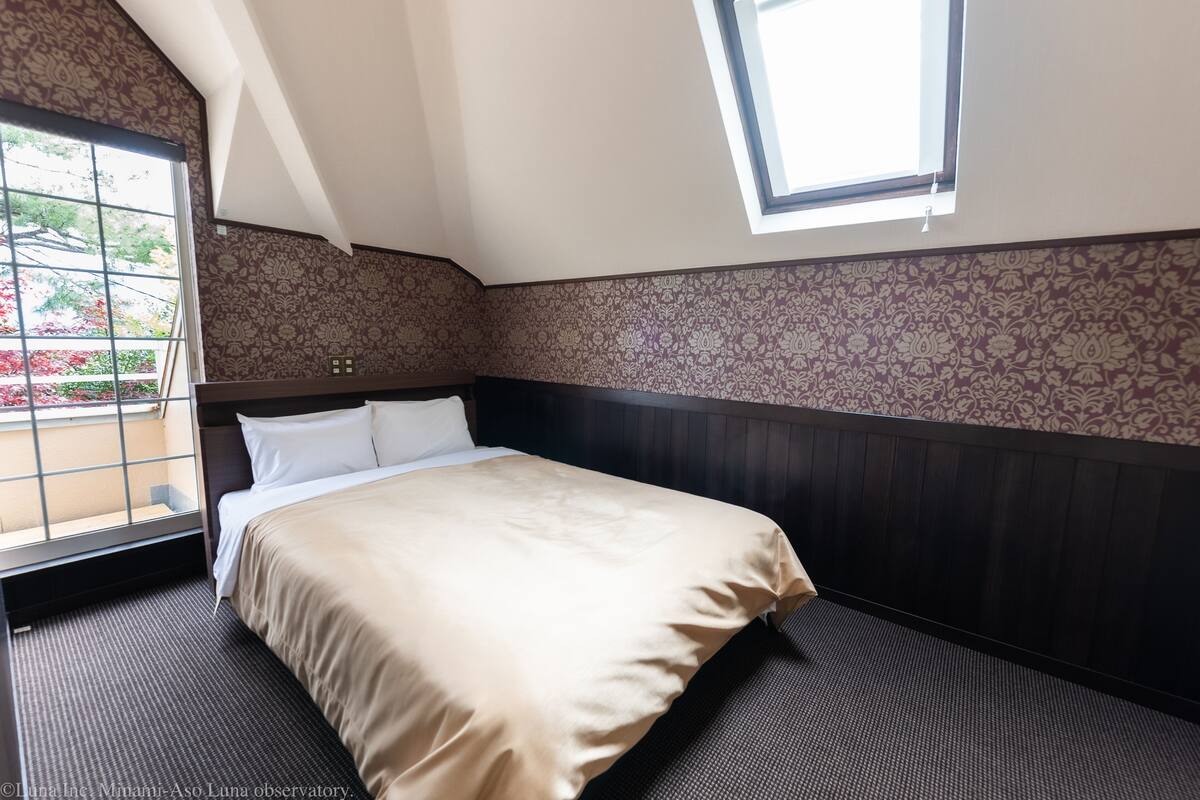 Habitación de hotel con una cama grande, una ventana con vistas a zonas verdes y papel tapiz estampado.