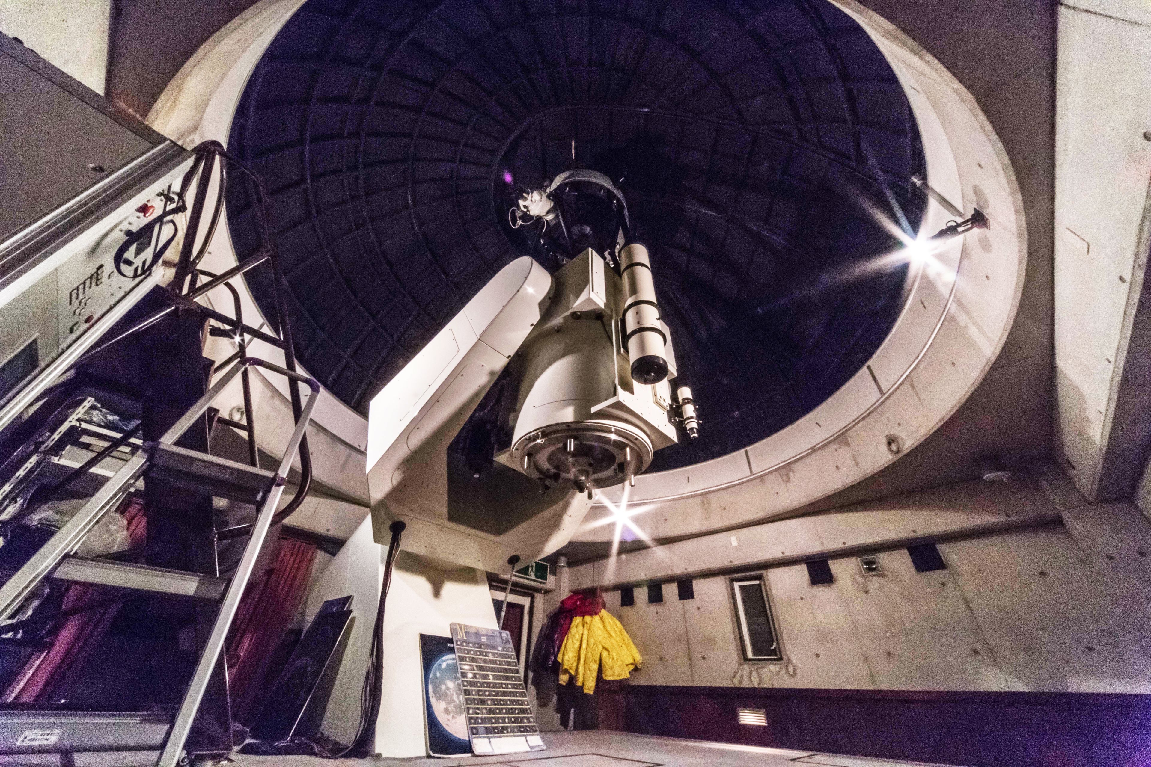 A telescope in a dome structure with a ladder and a control panel.