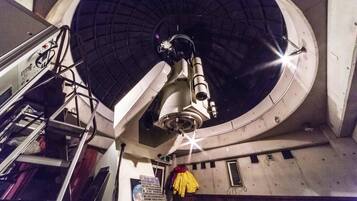 A telescope in a dome structure with a ladder and a control panel.