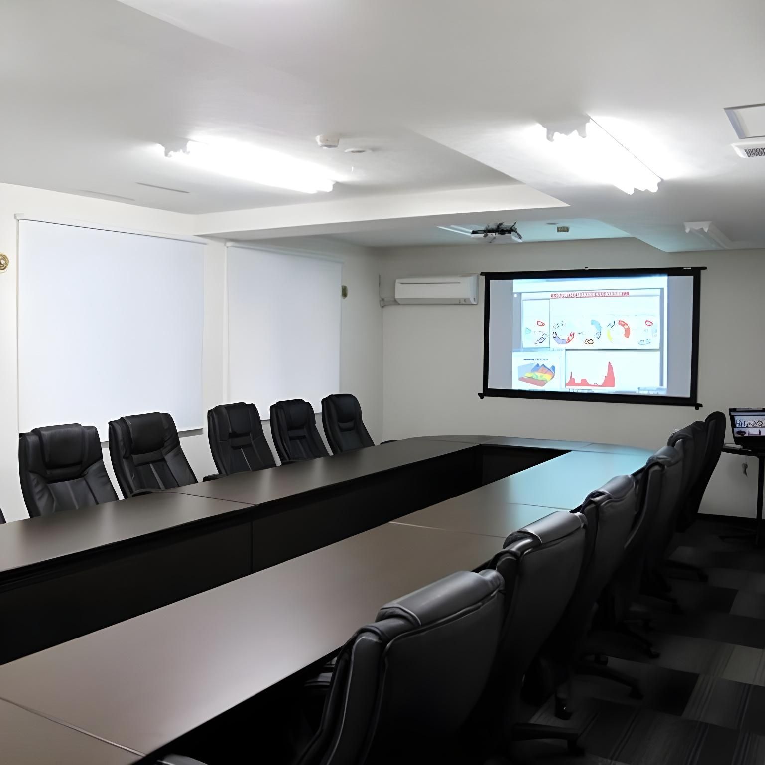 A conference room with a long table and six chairs, a projector screen, and an air conditioning unit on the wall.