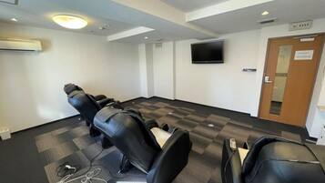 A conference room with a flat-screen TV mounted on the wall, a row of black chairs, and a check-in desk with a computer.