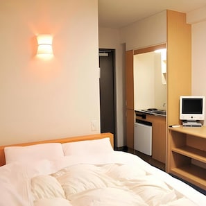 A hotel room with a bed, a desk with a computer, a mirror, and a wall-mounted light. - Hotel Housen Soka (Soka)