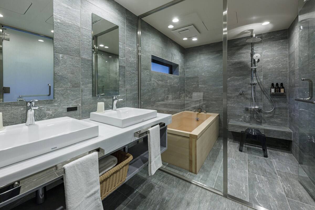 A modern bathroom with two sinks, a bathtub, and a glass-enclosed shower area.