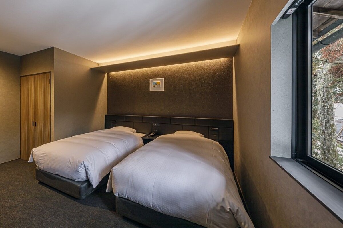 A hotel room with two beds, a window, and a door.