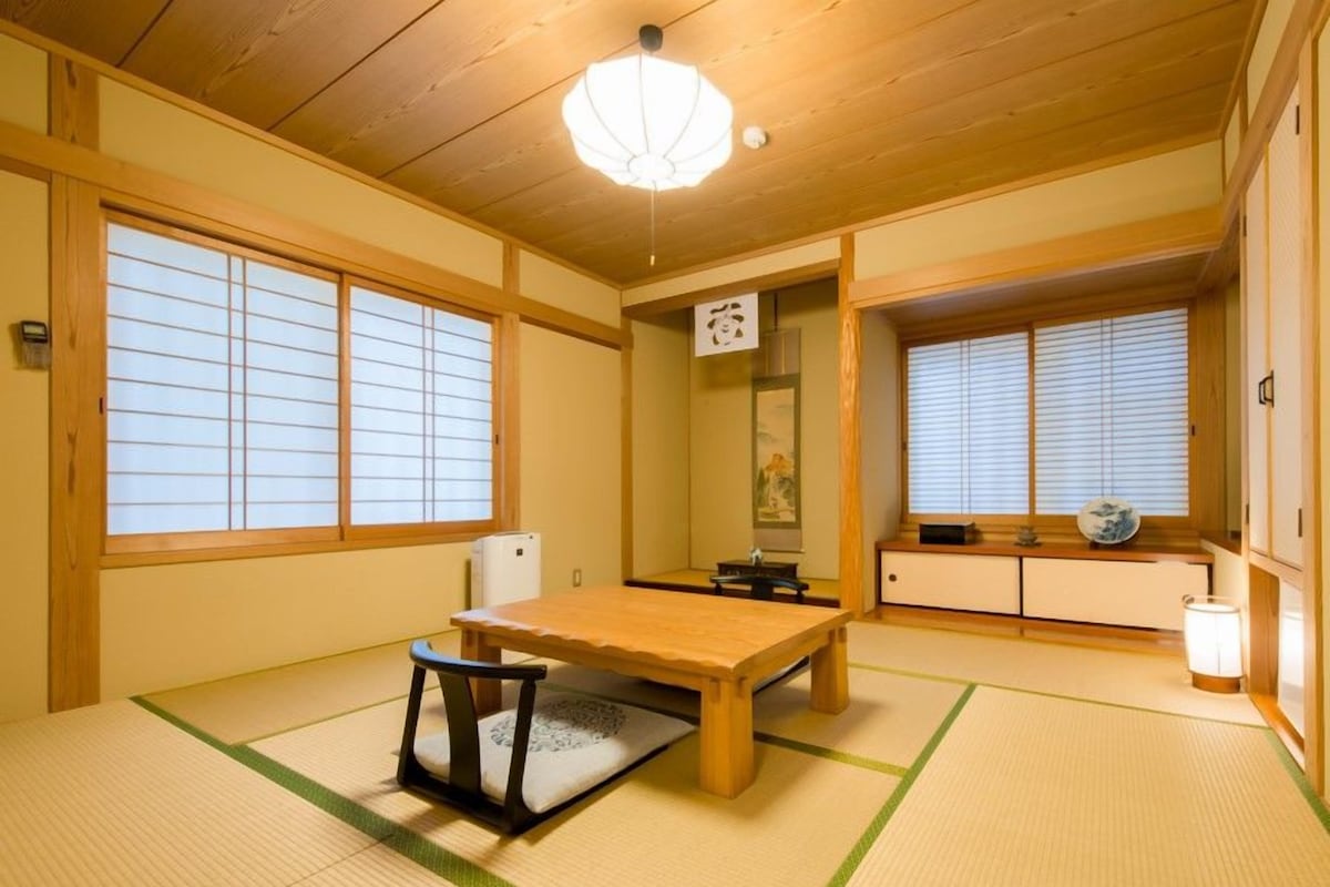 A traditional Japanese room with tatami flooring, a wooden table, a chair, sliding doors, and a ceiling light fixture.
