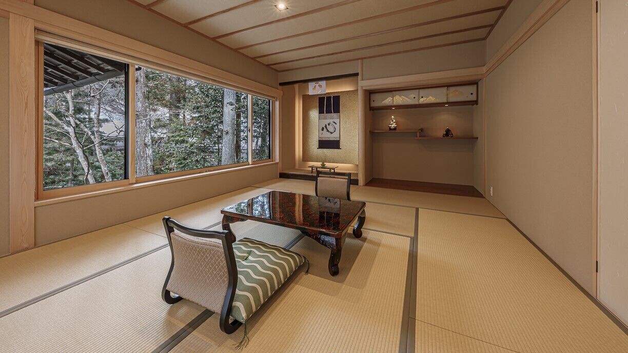 A tatami mat room with a low table, cushions, and a shelf with decorative items.