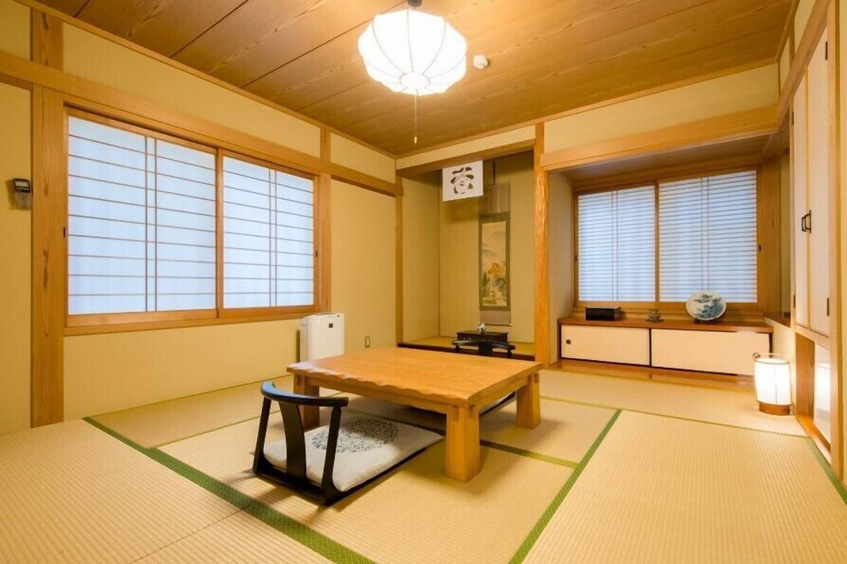 A traditional Japanese room with tatami flooring, a wooden table, a chair, sliding doors, and a ceiling light fixture.