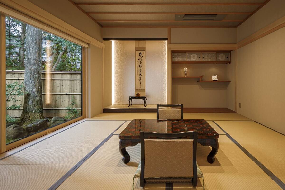 A traditional Japanese room with tatami flooring, a low table, a chair, and a sliding door leading to a garden.