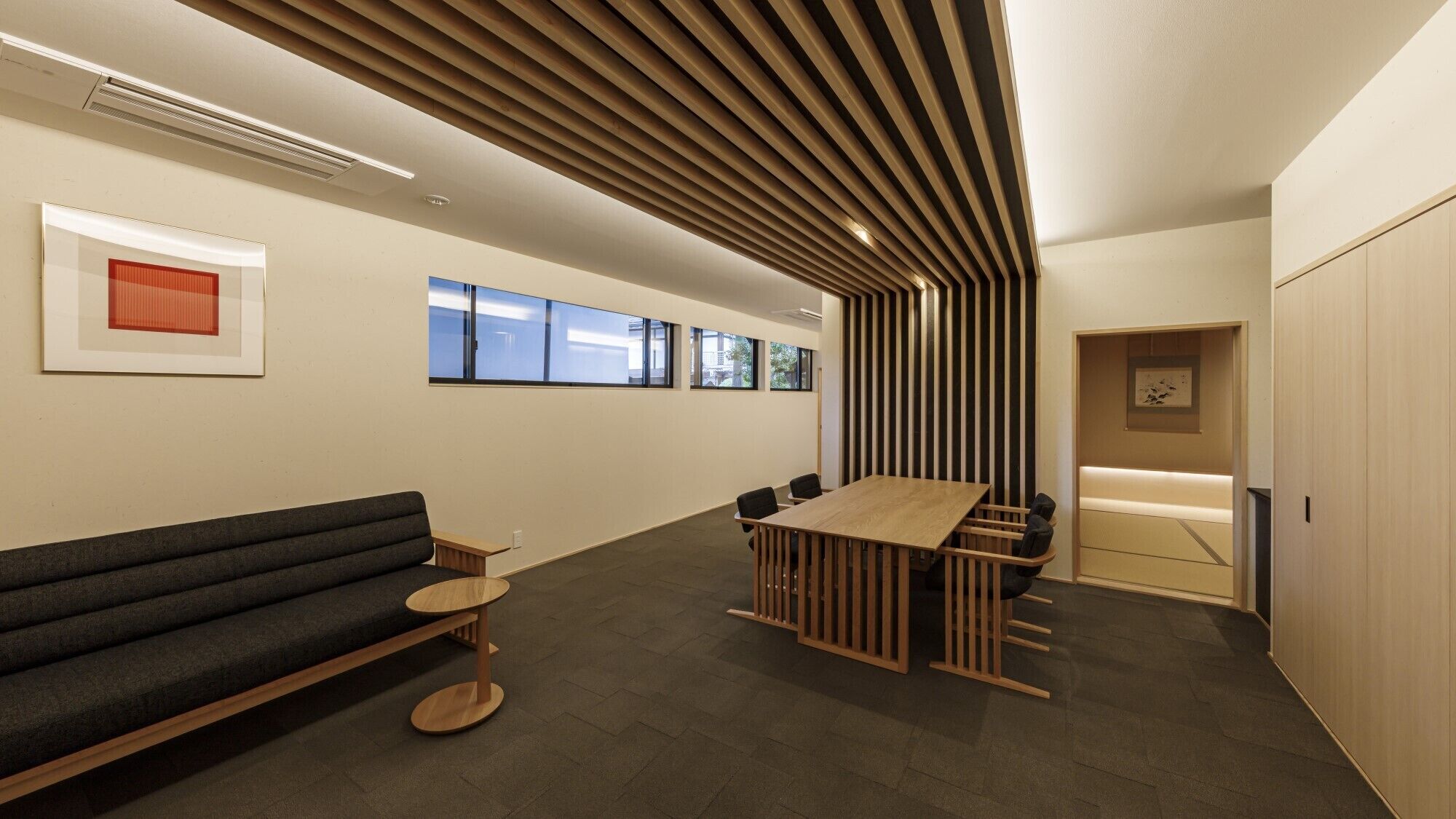 A modern office space with a long table, a sofa, and a wooden slatted ceiling.