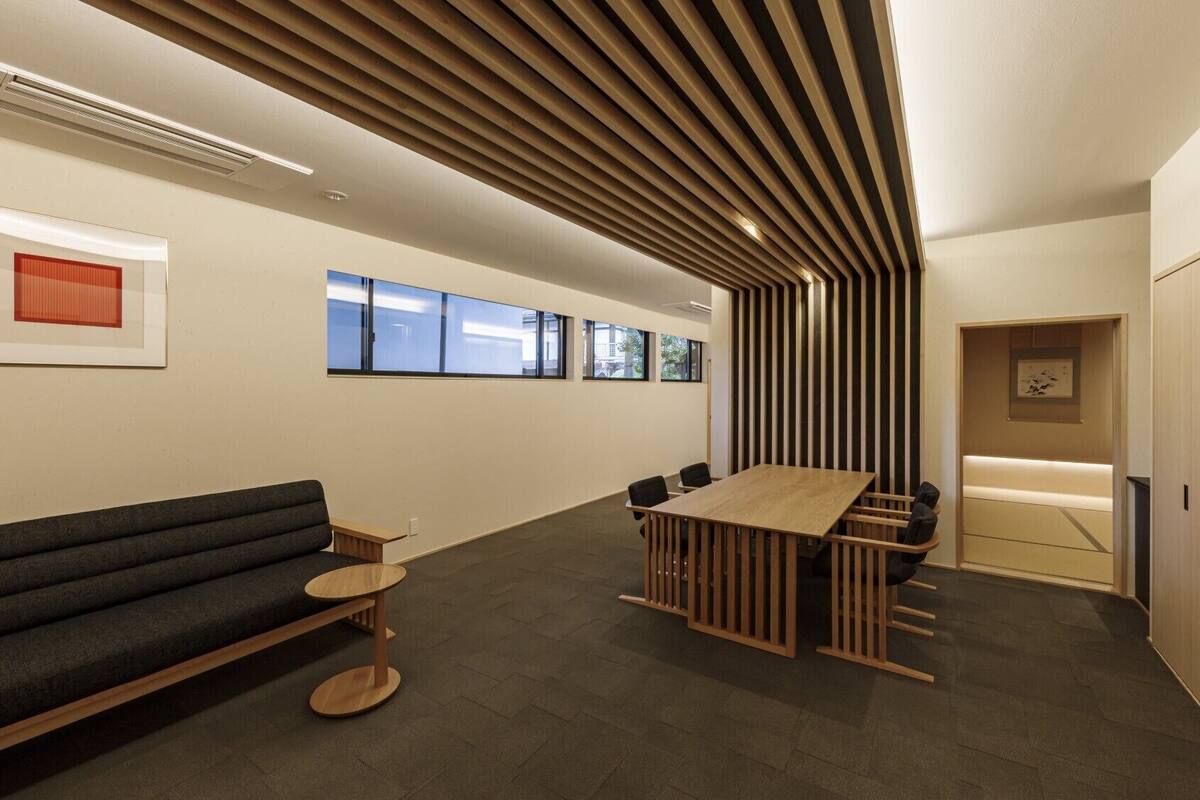 A modern office space with a long table, a sofa, and a wooden slatted ceiling.