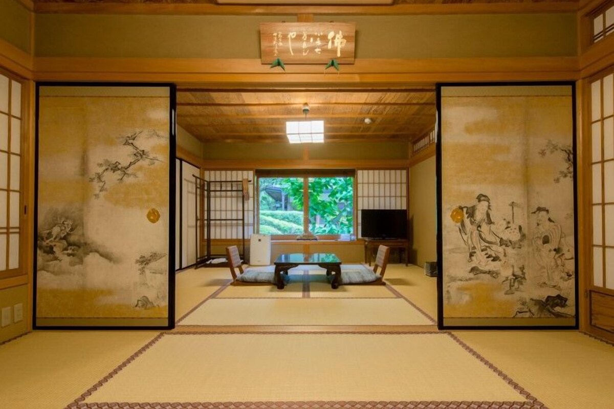Une pièce de style japonais traditionnel, avec un sol recouvert de tatamis, un téléviseur et des œuvres d’art accrochées aux murs.