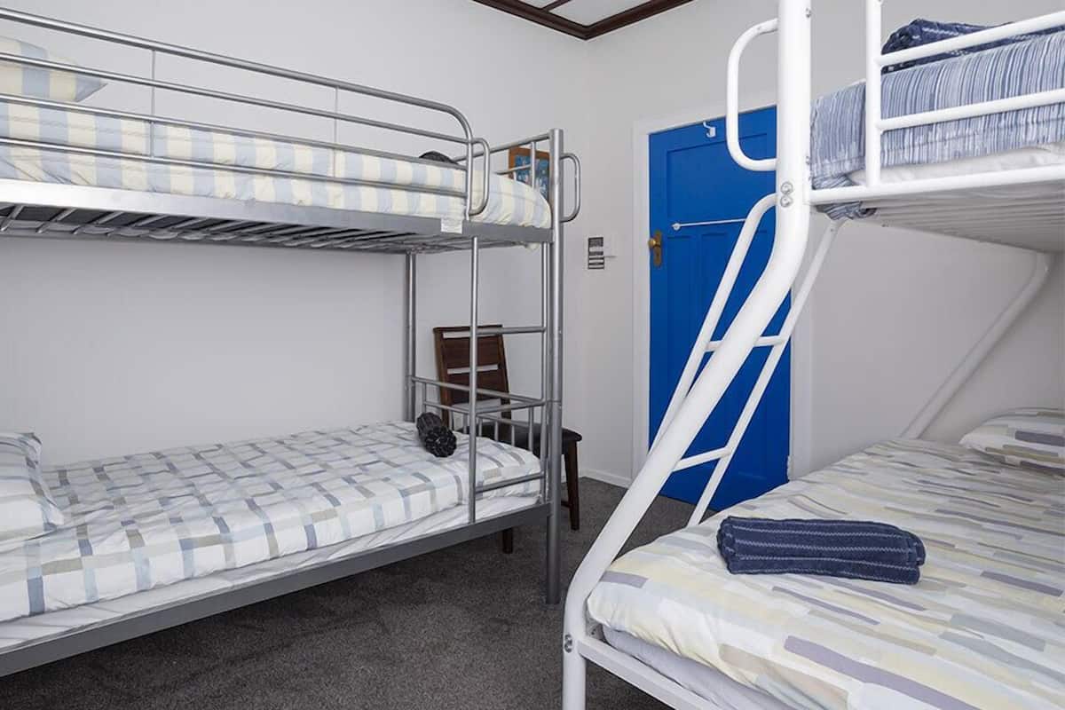 A bunk bed room with a blue door, a chair, and a small table.