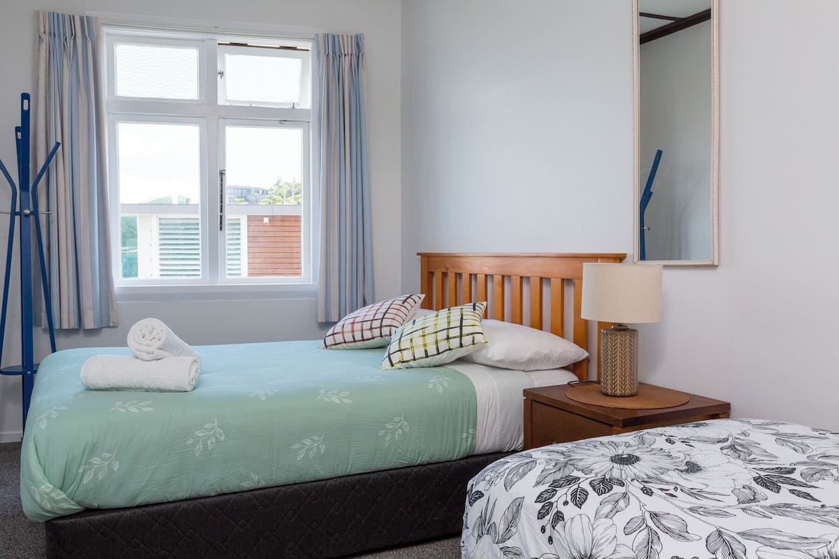 A bedroom with a bed, a nightstand, a mirror, and a window with curtains.