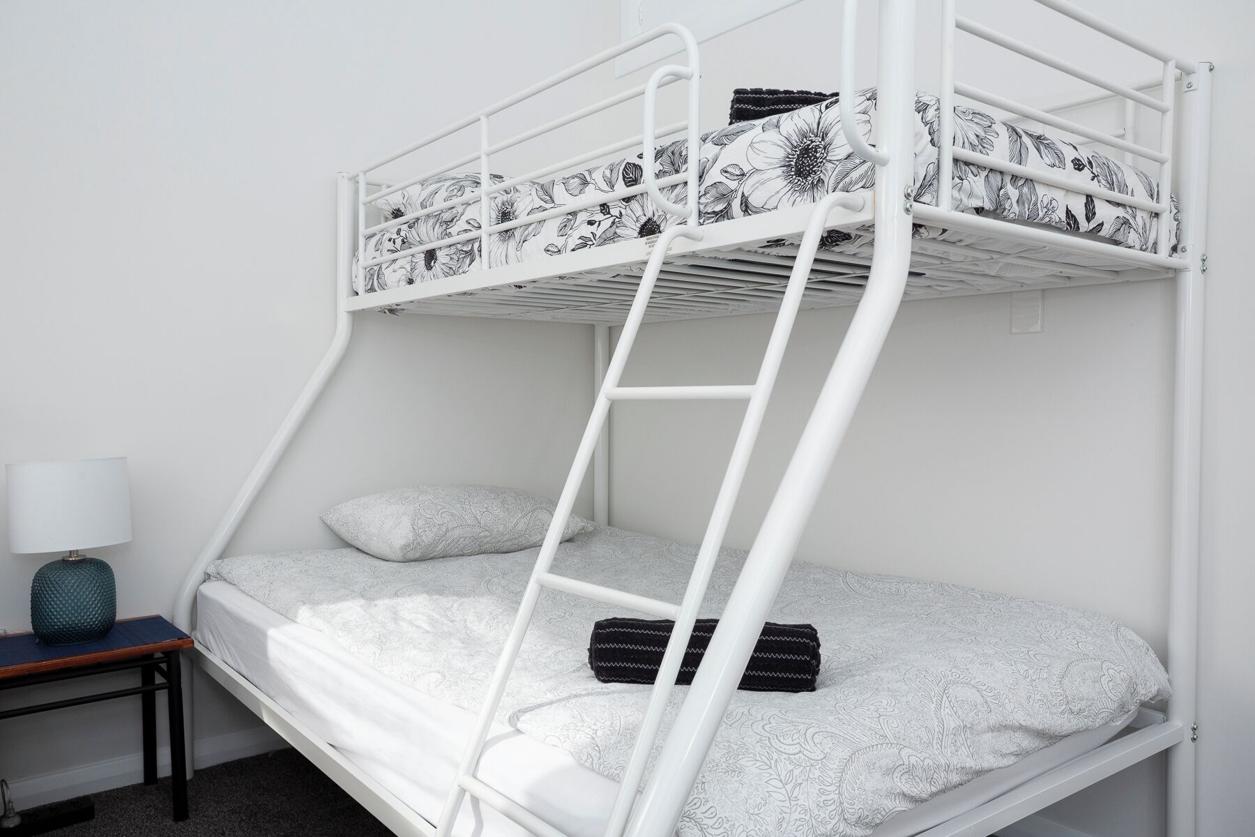 Una litera con escalera, una mesita de noche con lámpara y ropa de cama estampada.