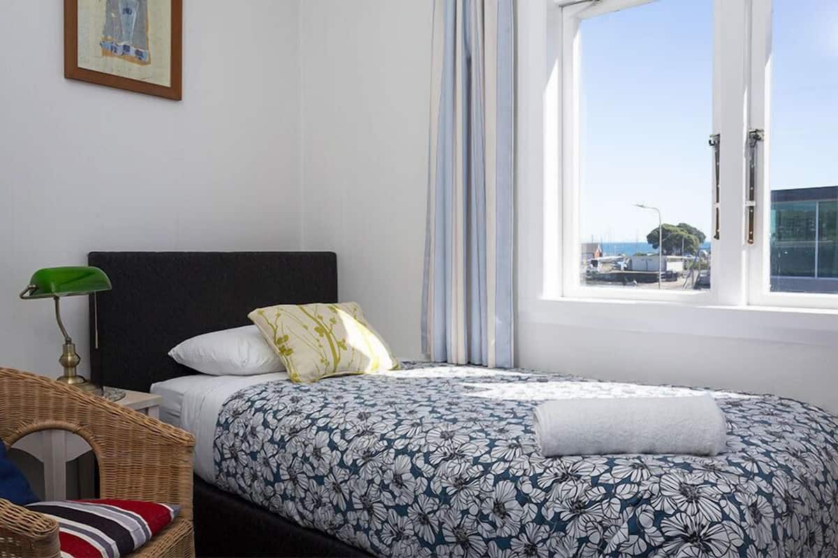 A bedroom with a bed, a wicker chair, a lamp, and a window with curtains.