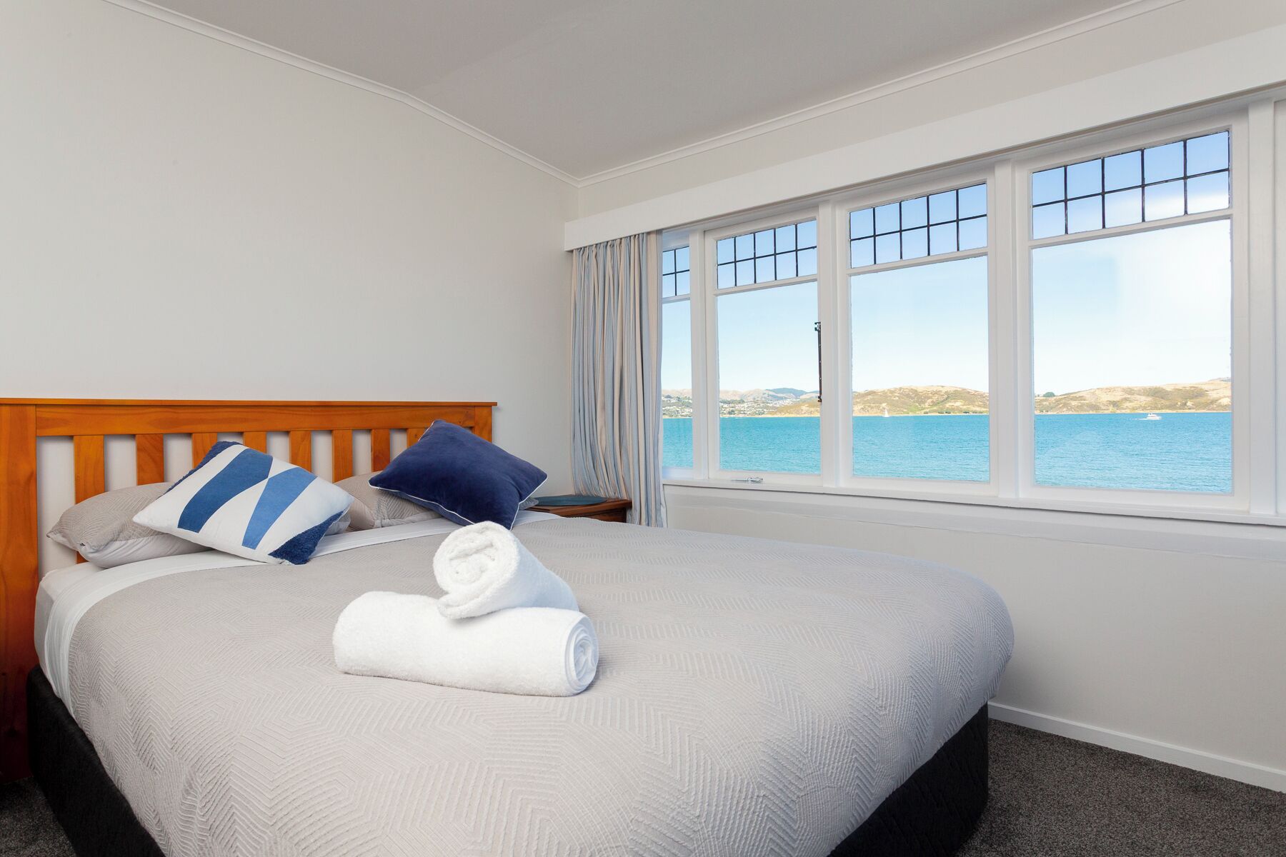 A hotel room with a bed, a view of the sea, and a window with curtains.