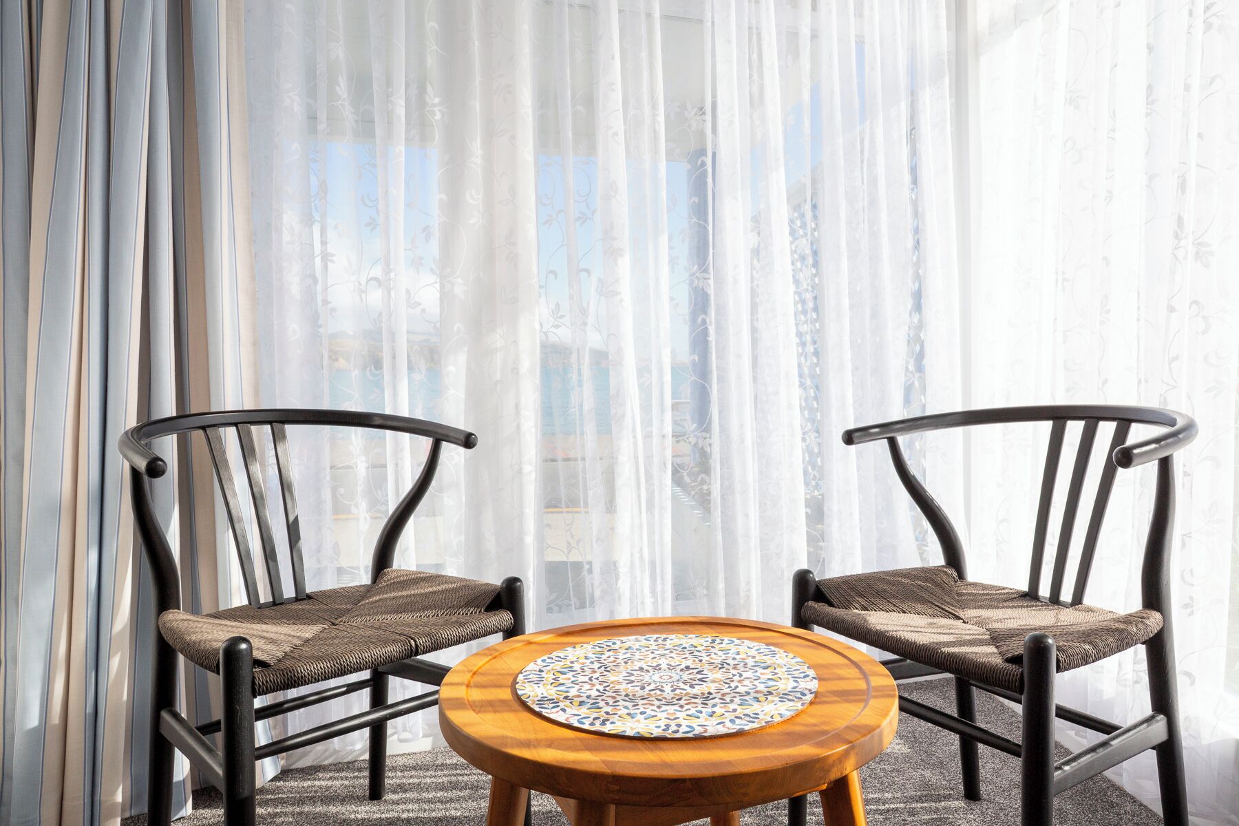 Two wicker chairs with cushioned seats and backs, positioned around a round wooden table with a patterned table runner.