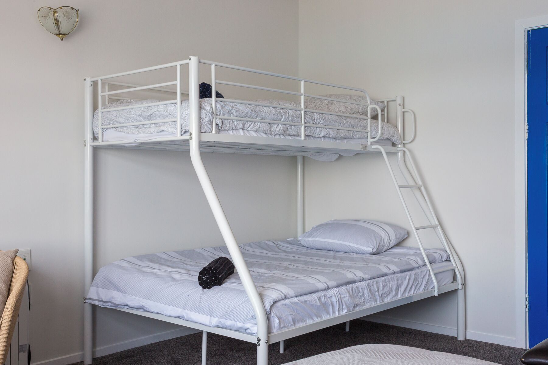 Un letto a castello con una scala, un letto singolo in basso e una porta blu sullo sfondo.