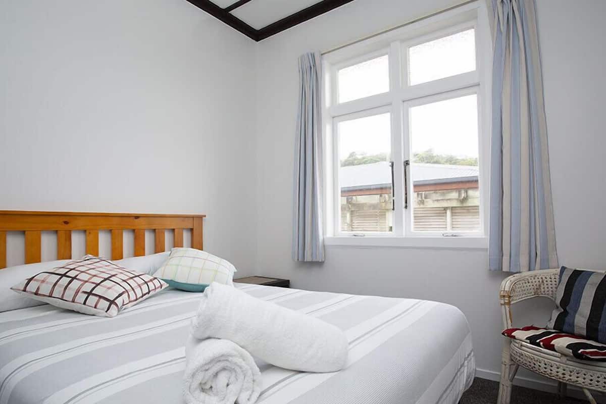 A neatly made bed with striped bedding, a wooden headboard, and a rolled white towel.