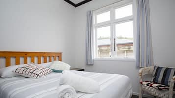 A neatly made bed with striped bedding, a wooden headboard, and a rolled white towel.