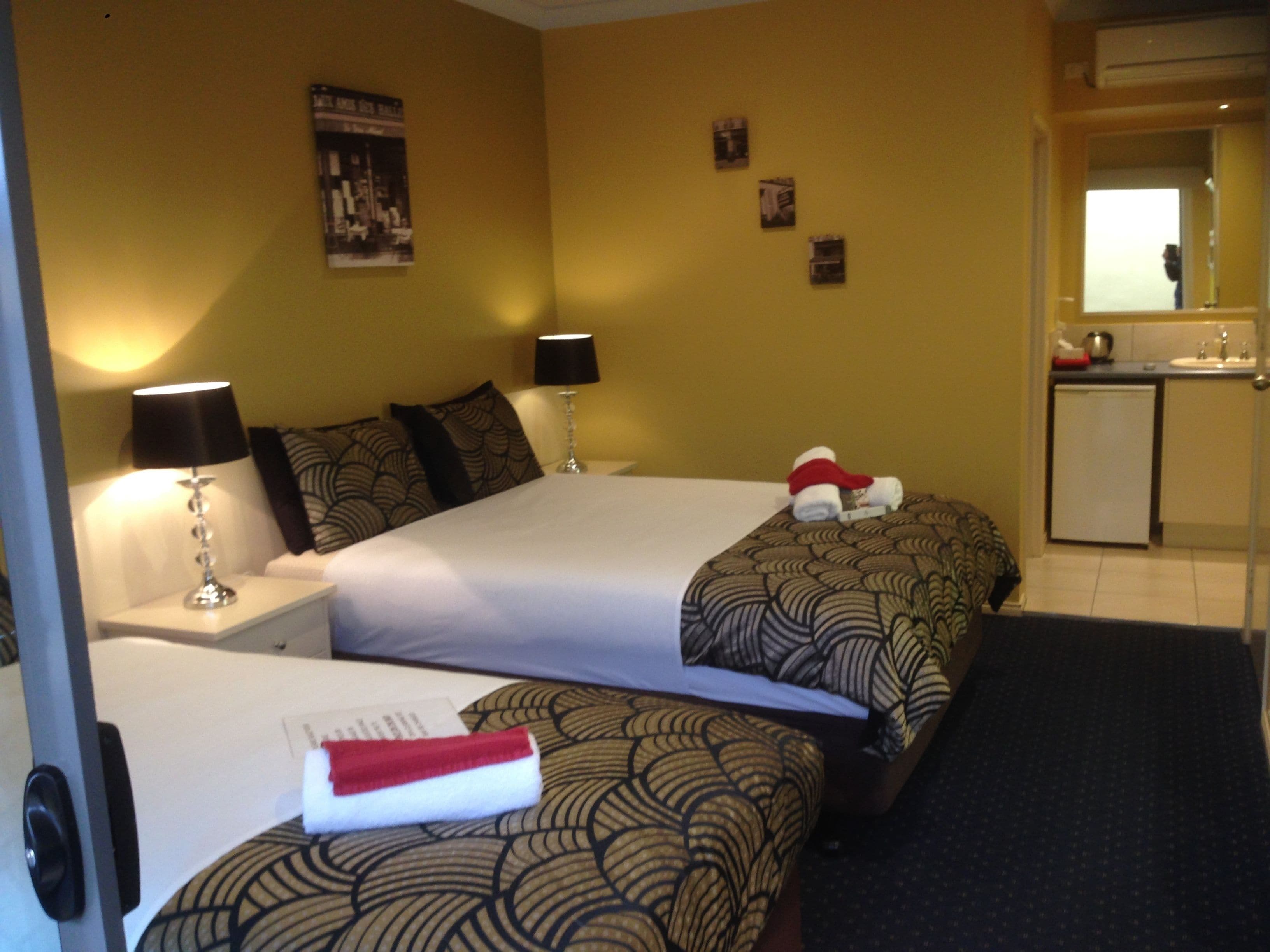 Quarto de hotel com duas camas, uma escrivaninha, um abajur, uma kitchenette pequena e um banheiro.