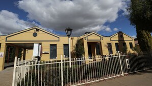 Un bâtiment jaune avec une clôture blanche, une pancarte indiquant qu’il y a des places disponibles et un lampadaire.