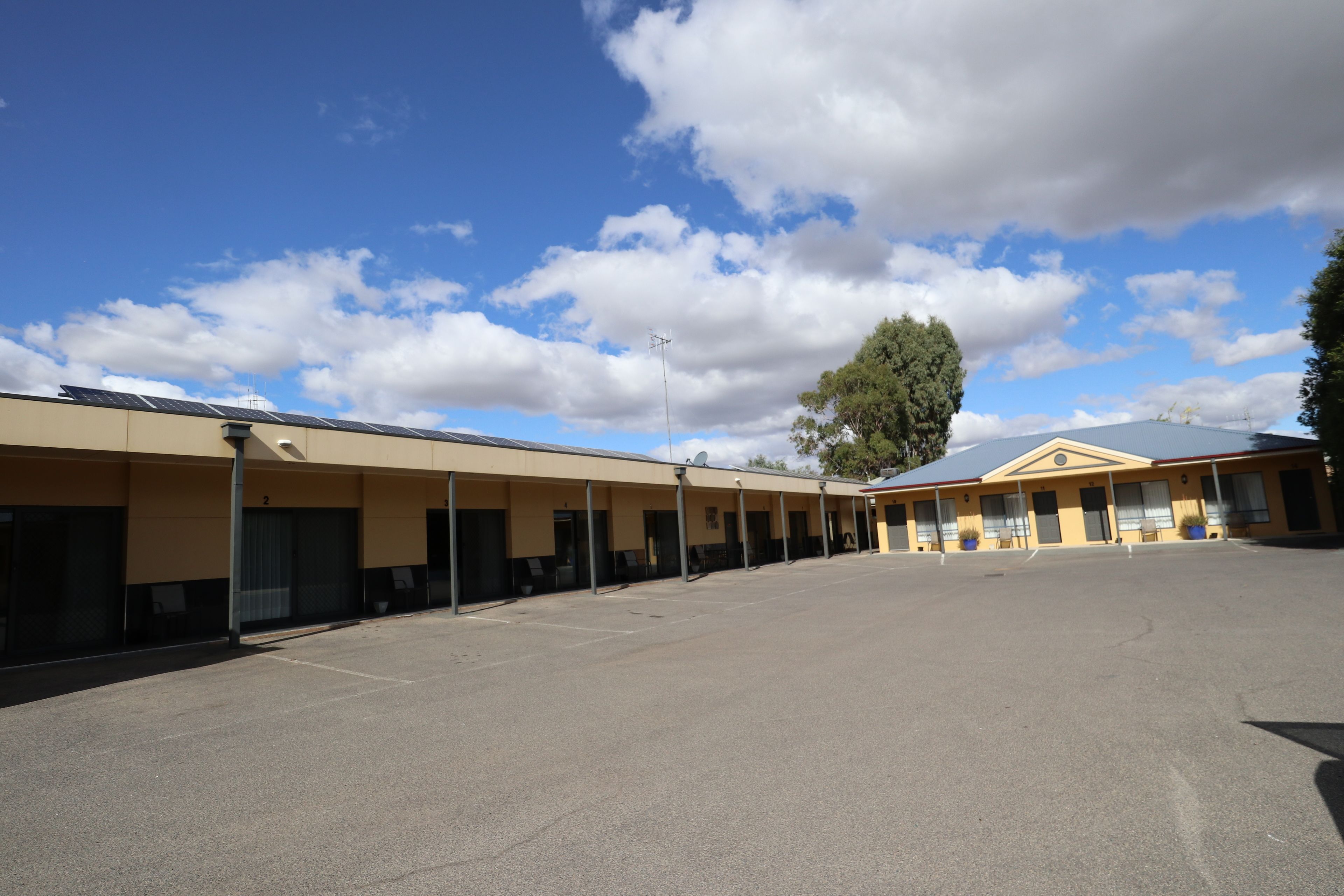 A motel with a long row of rooms, a large parking lot, and a clear blue sky with clouds.