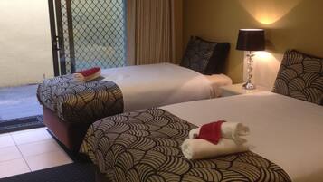 A hotel room with two beds, a sliding glass door to the balcony, a wall-mounted lamp, and a small picture frame.