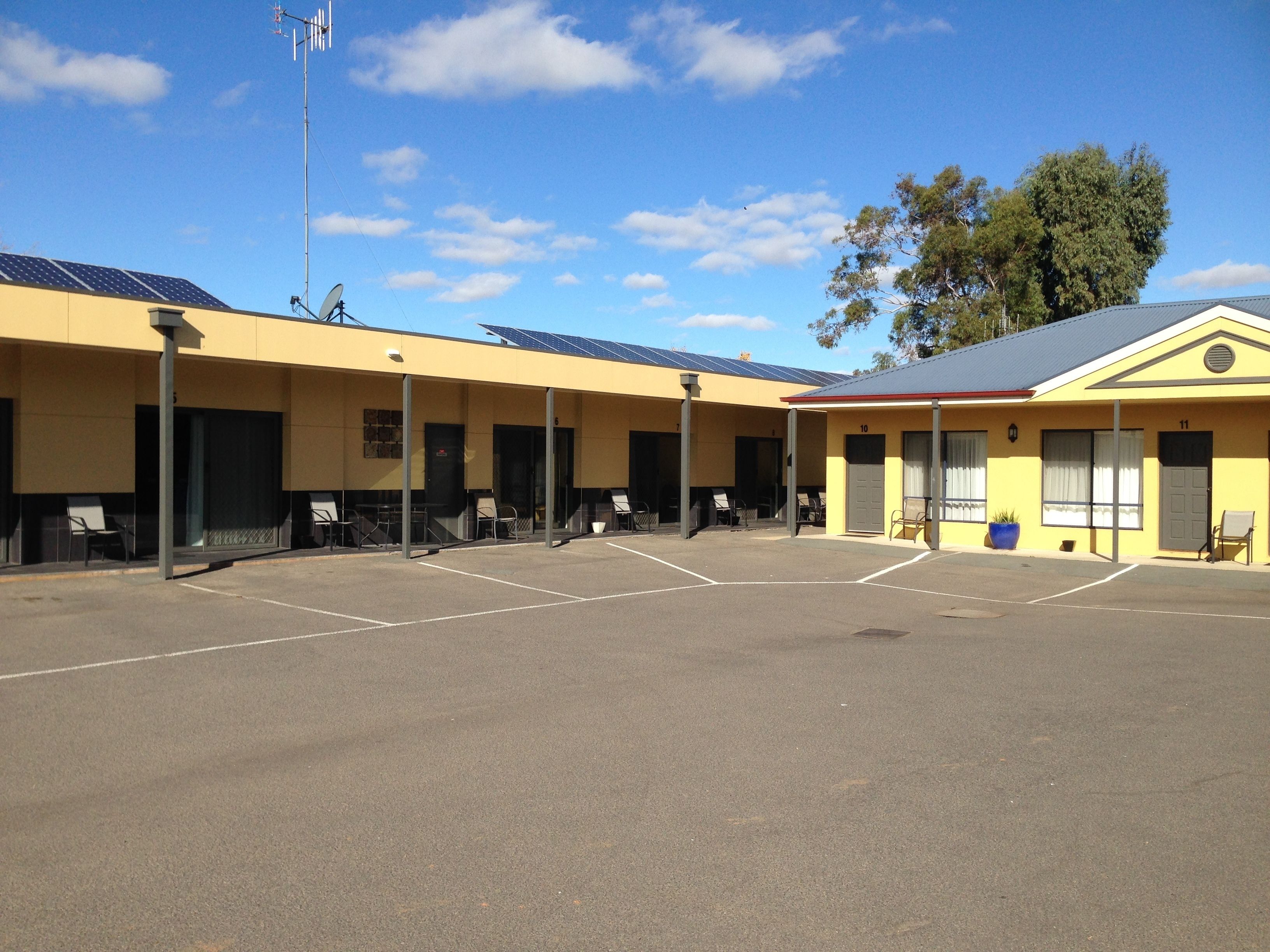 A motel with a row of rooms, each with a door and windows, and a parking lot in front.