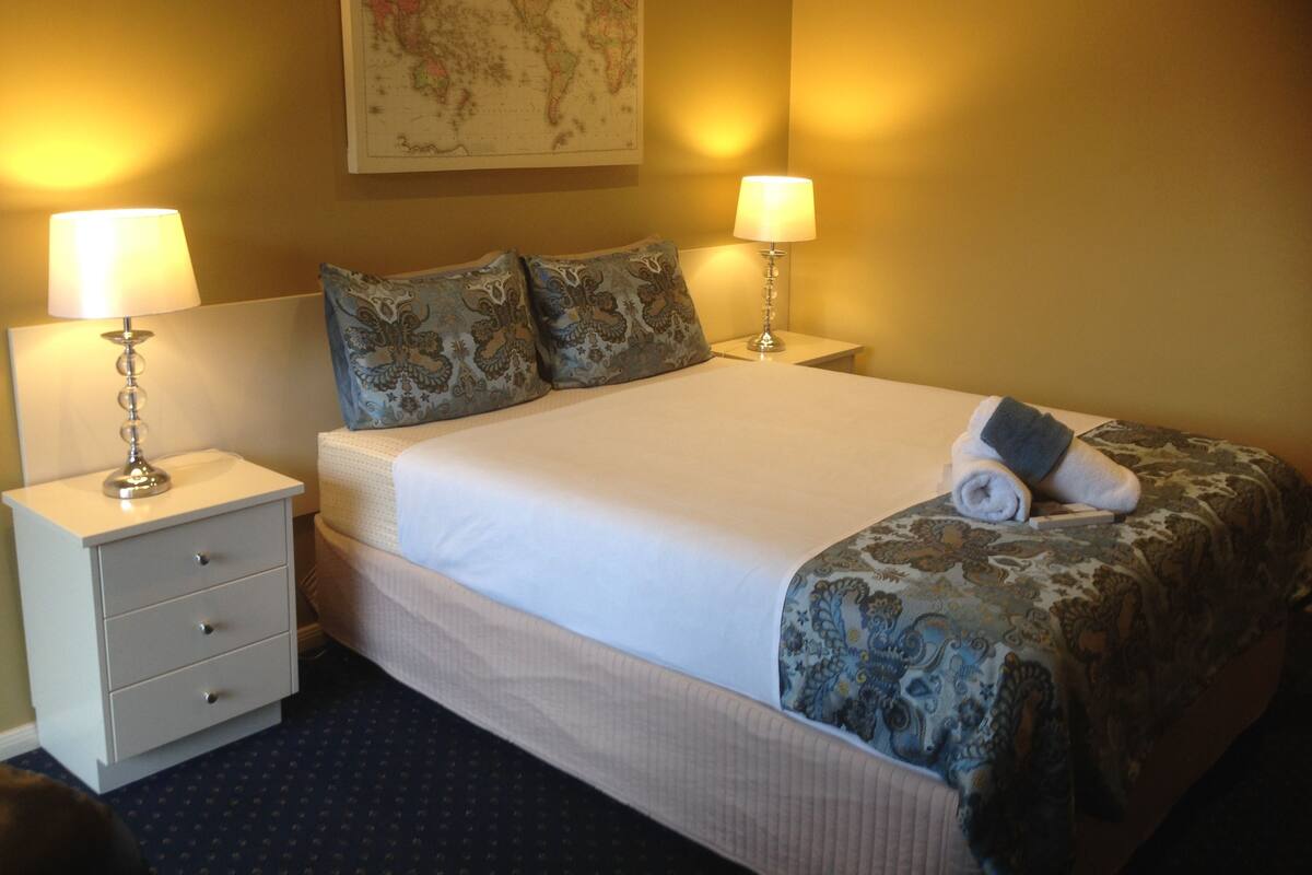 A neatly made bed with a white duvet, two matching lamps on side tables, and a world map on the wall.