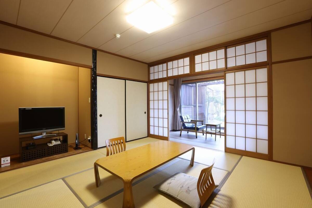 A traditional Japanese room with tatami flooring, a low table, chairs, a television, and sliding doors.