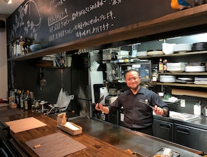 A kitchen with a blackboard menu, stainless steel appliances, and a counter with a basket and mat. - Miyahama Onsen Miyahama Grand Hotel (Hatsukaichi)