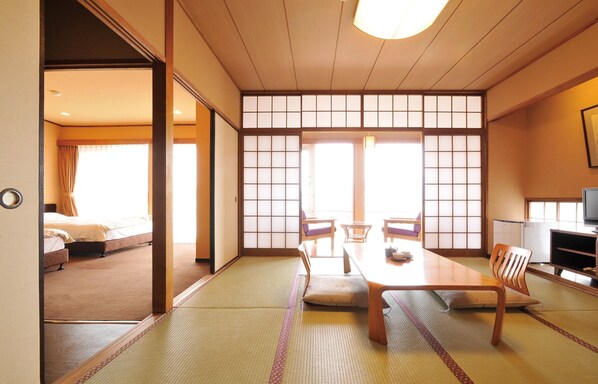 A traditional Japanese room with tatami flooring, a low table with cushions, sliding doors, and a television. - Miyahama Onsen Miyahama Grand Hotel (Hatsukaichi)