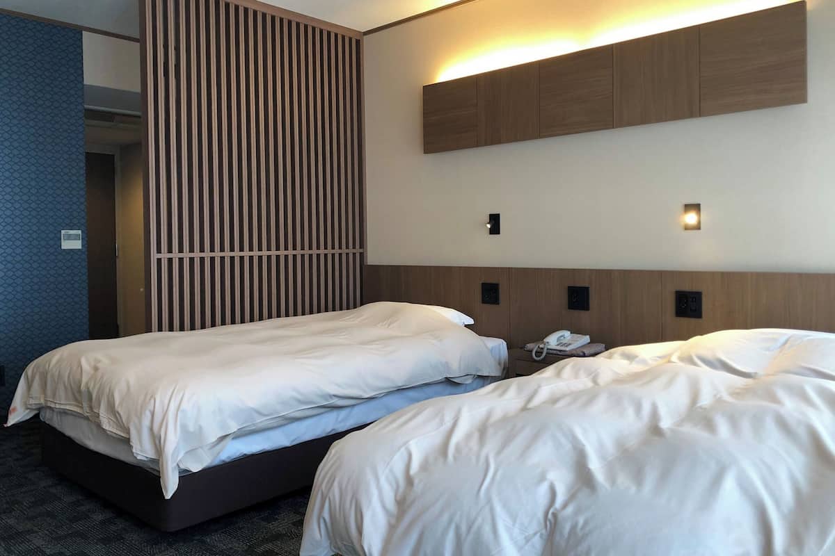 A hotel room with two beds, a vertical wooden panel, a wall-mounted phone, and a light fixture.