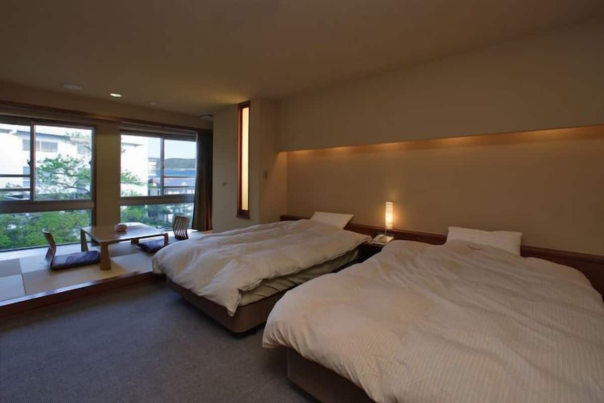 A hotel room with two beds, a small table, and a chair by the window.