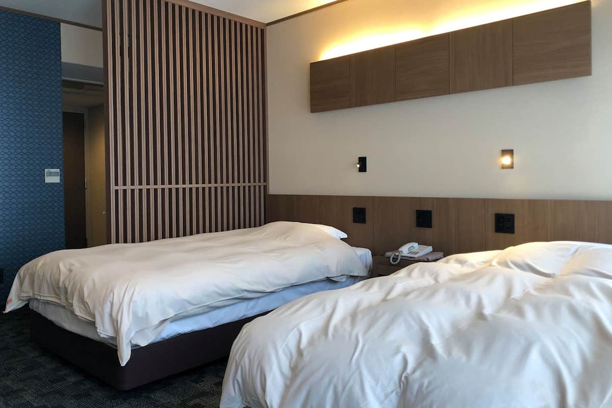 A hotel room with two beds, a wooden panel wall, and a built-in desk with a phone.