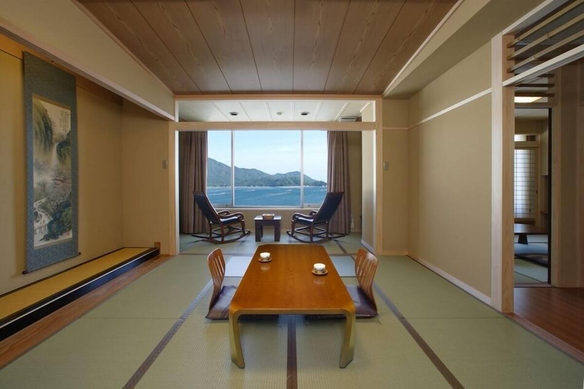 A traditional Japanese-style room with tatami flooring, a low wooden table, and a view of the sea.