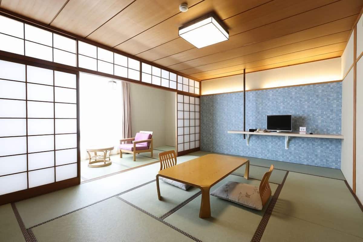 A traditional Japanese room with tatami flooring, a low table, a television on a shelf, and a sliding door.