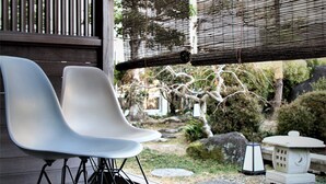 A wooden deck with two white chairs, a bamboo screen, and a view of a garden with a stone lantern. - Miyahama Onsen Miyahama Grand Hotel (Hatsukaichi)